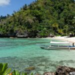 Labuan Bajo coastline with traditional boat and clear waters.